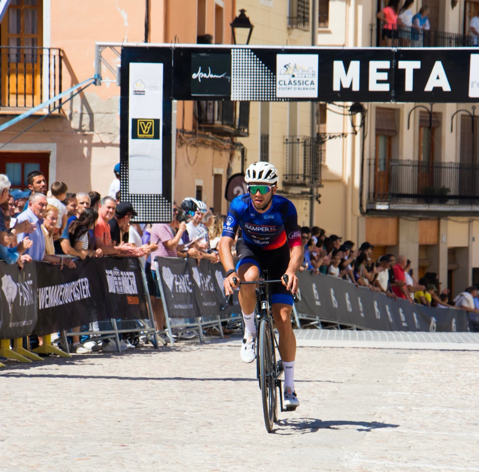 Ciclista cruzando la línea de meta de una carrera, con público a los lados